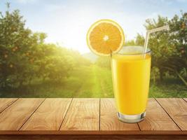 Fresh orange juice with on wooden table and orange plantation with fruits in sun light photo