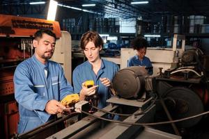 Asian male and White female engineer workers in safety uniforms work by inspecting machines' voltage current, checking, and maintaining at manufacturing factory, electric system service occupations. photo