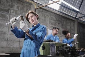 joven trabajadora de la industria caucásica trabaja con herramientas de precisión de metalistería, máquinas de torno y taller de piezas de repuesto con un equipo multirracial en la fábrica de fabricación, ingenieros mecánicos profesionales. foto