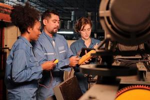 Los equipos multirraciales de ingenieros de la industria profesional con uniformes de seguridad trabajan inspeccionando la corriente de voltaje de las máquinas, comprobando y manteniendo en la fábrica de fabricación, ocupaciones de servicio del sistema eléctrico. foto