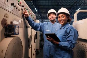 retrato de dos ingenieros profesionales de la industria asociados con cascos y uniformes de seguridad mirando la cámara y sonriendo, inspeccionando y manteniendo la máquina de control en la fábrica de fabricación, ocupación de servicio. foto