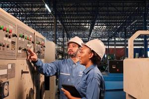 Professional industry engineer partner in hard hats and safety uniforms inspect machine's control panel, maintenance check with tablet in mechanical manufacture factory, electrical service occupation. photo