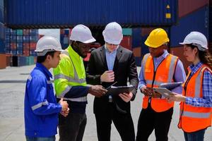 Group of multiracial workers in safety uniforms and hardhats work at logistics terminal dock with stacks of containers, loading control, and management shipping goods, cargo transportation industry. photo