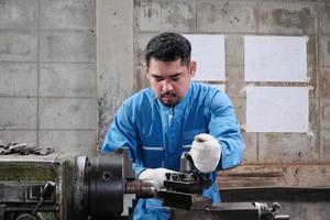 One professional Asian male industry engineer worker works in a safety uniform with metalwork precision tools, mechanical lathe machines, and spare parts workshop in the steel manufacturing factory. photo