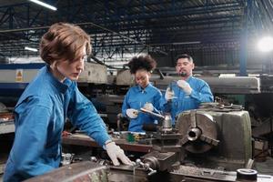 Young Caucasian female industry worker works with metalwork precision tools, lathe machines, and spare parts workshop with multiracial team in manufacturing factory, professional mechanical engineers.