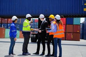 Group of multiracial workers in safety uniforms and hardhats work at logistics terminal dock with stacks of containers, loading control, and management shipping goods, cargo transportation industry. photo
