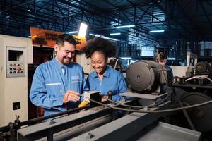 Asian male and female African American engineers in safety uniform work by inspecting machines' voltage current, checking, and maintaining at manufacture factory, electric system service occupations. photo