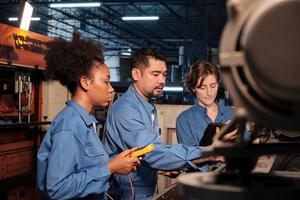 Multiracial professional industry engineer teams in safety uniforms work by inspecting machines' voltage current, checking, and maintaining at manufacture factory, electric system service occupations. photo