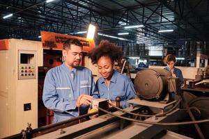 Asian male and female African American engineers in safety uniform work by inspecting machines' voltage current, checking, and maintaining at manufacture factory, electric system service occupations. photo