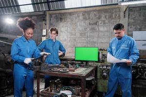 tres equipos de trabajadores de ingeniería de la industria profesional multirracial en trabajos de metalurgia de uniformes de seguridad discuten cerca del monitor de pantalla verde, máquinas de torno mecánico y taller en la fábrica de fabricación. foto