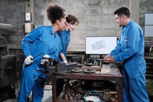 Three multiracial professional industry engineer workers teams in safety uniforms metalwork jobs discuss with mechanical drawing in a monitor, lathe machines, and workshop in manufacturing factory. photo