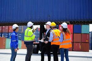 Group of multiracial workers in safety uniforms and hardhats work at logistics terminal dock with stacks of containers, loading control, and management shipping goods, cargo transportation industry. photo