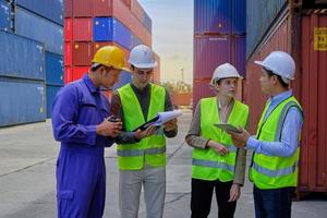 un grupo de trabajadores multirraciales con uniformes de seguridad y cascos trabajan en la terminal logística con muchas pilas de contenedores, control de carga y envío de mercancías para la industria del transporte de carga. foto