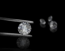 Diamond in tweezers on a black background with diamonds group soft focusing photo