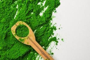 Close up of green powder and wooden spoon on white background. photo