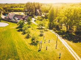 Aerial view group of young caucasian friends enjoy playing volleyball on grassy area in Lithuania countryside photo