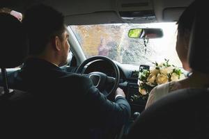 Interior front seat view bride and groom sit in car while friends spray sparkling wine on car . Culture and wedding celebrations in Lithuania photo