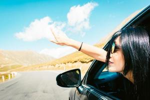 Female caucasian woman from car window points finger up left with asphalt road background. Copypaste road trip concept. photo