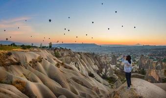 teléfono inteligente en manos de una mujer tomando fotos de un hermoso paisaje y globos en capadocia. hora del amanecer, concepto de viaje de ensueño