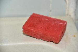 Red sponge for cleaning in a dirty bathroom on the washbasin photo