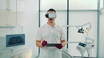 Vorderansicht des jungen Zahnarztes mit Touchscreen und Virtual-Reality-Brille. männlicher kaukasischer arzt, der an einer holografischen schnittstelle mit einer zahnärztlichen einheit im hintergrund arbeitet. Konzept der digitalen Technologie video