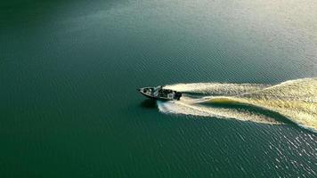 boven weergave van motorbootroutes op het blauwe zeeoppervlak. zijaanzicht van een speedmotorboot die op donker zeewater vaart, witte wervelsporen achterlatend in de zomerschemering. concept van wateractiviteiten video