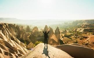 Female person stand with hands up over dramatic valley on hazy sunrise with fairy chimneys background. Solo exploration in Turkey. Cinematic Travel destination-Cappadocia 2020.
