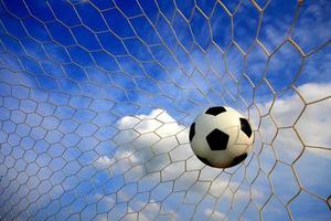 símbolo de éxito y victoria para el balón de fútbol clásico tiene color blanco y negro entrando en la red de gol después de disparar en el juego con un fondo de cielo azul. concepto de éxito. foto