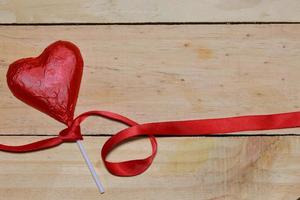 Chocolate heart wrapped in red and Red Ribbon on wood. valentine concept. Space for text. photo