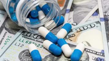 pastillas de cápsula azul blanco con un frasco en el dinero, dólares americanos. movimiento dinámico. medicina y negocios video