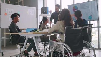 un employé handicapé de l'entreprise est capable de travailler de manière agréable avec ses collègues au bureau. un groupe de commerçants ont une discussion lors de la réunion. video