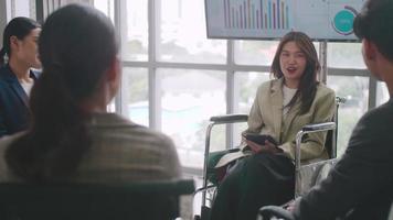 Confident business woman in wheelchair presenting during business meeting with colleagues. Asian business team celebrating success together in boardroom. video