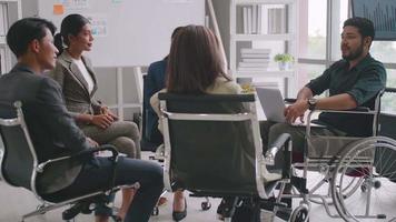 hombre de negocios confiado en silla de ruedas que presenta durante una reunión de negocios con colegas. equipo de negocios asiático celebrando el éxito juntos en la sala de juntas. video