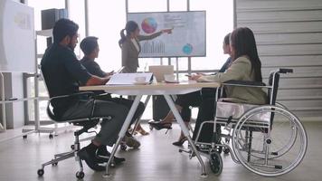 un employé handicapé de l'entreprise est capable de travailler de manière agréable avec ses collègues au bureau. un groupe de commerçants ont une discussion lors de la réunion. video