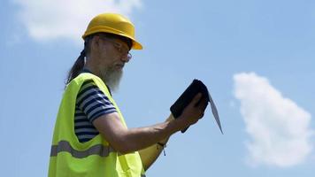 Port Worker With A Beard In A Yellow Helmet Stands With A Tablet PC. The Foreman Inspects. 4K video