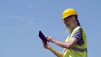 Hafenarbeiter mit Bart in einem gelben Helm steht mit einem Tablet-PC. der Vorarbeiter kontrolliert. 4k video