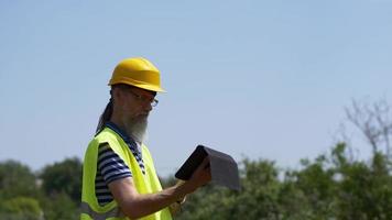 travailleur portuaire avec une barbe dans un casque jaune se tient avec une tablette pc. le contremaître inspecte. 4k video