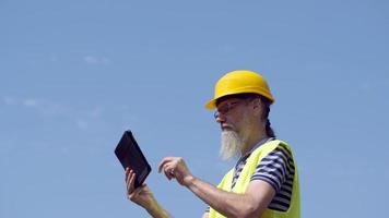 lavoratore portuale con la barba in un casco giallo sta con un tablet pc. il caposquadra ispeziona. 4k video