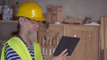 travailleur portuaire avec une barbe dans un casque jaune se tient avec une tablette pc. le contremaître inspecte. 4k