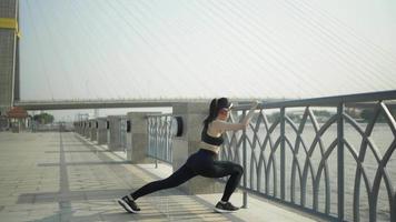 mulheres atletas asiáticas em câmera lenta usam roupas esportivas em alongamento preto. aquecer antes de correr uma maratona prática todos os dias de manhã na cidade com o rio antes da maratona. video