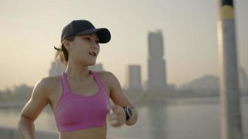 Woman on a morning jog. Following slow motion back view. Fitness runner training. Sunny sky with clouds at sunset or sunrise. Jogger on dock by the lake. Sport motivation. video