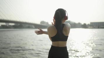 slow-motion aziatische atleet vrouwen dragen sportkleding in zwarte stretching. opwarmen voordat je elke dag een marathonoefent in de stad met de rivier voor de marathon. video