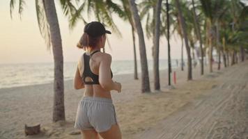 woman running ocean beach. Young asian female exercising outdoors running seashore. Concept of healthy running and outdoor exercise. Active, sporty athlete jogging. Summer active video