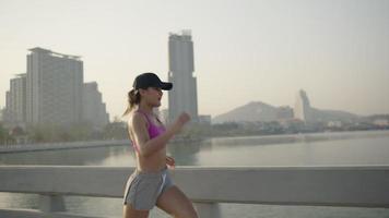 Woman on a morning jog. Following slow motion back view. Fitness runner training. Sunny sky with clouds at sunset or sunrise. Jogger on dock by the lake. Sport motivation.