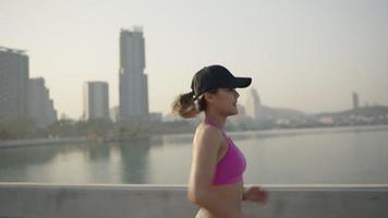 vrouw op een ochtend joggen. volgende slow motion achteraanzicht. fitness loper opleiding. zonnige hemel met wolken bij zonsondergang of zonsopgang. jogger op dok bij het meer. sportieve motivatie. video