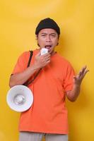 Asian young man in casual style is  frowning while using megaphone isolated on yellow background. photo