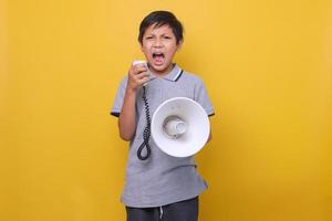 Cute Asian boy yelling on megaphone againts yellow background photo