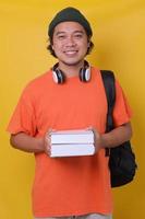 Asian young man in casual style with backpack and headphone bringing books isolated on yellow background. School college university concept. photo