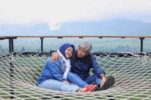 Asian elderly couple chill on net with view of tea plantation and mountain. photo