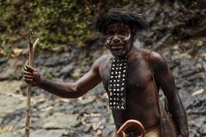 hombre de la tribu dani de papua indonesia vestido con traje tradicional y koteka cruzando el río. foto